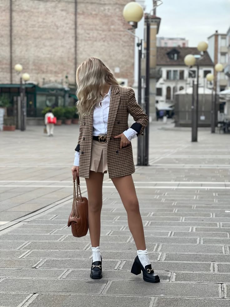 A confident woman wears a tailored plaid blazer dress with chunky heeled loafers. The look is structured, smart, and perfect for a bold fall statement.