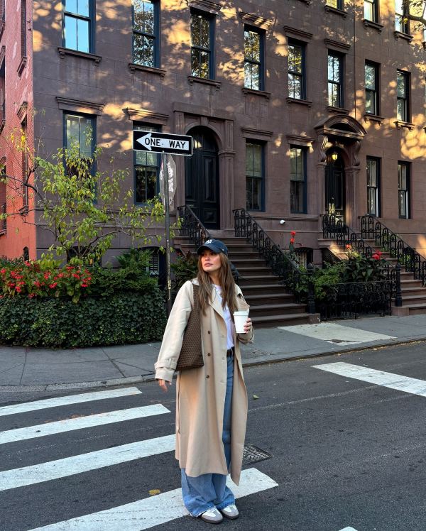 A stylish woman walks confidently down a New York street in a camel coat, black turtleneck, and wide-leg trousers. The outfit exudes timeless elegance and quiet luxury.